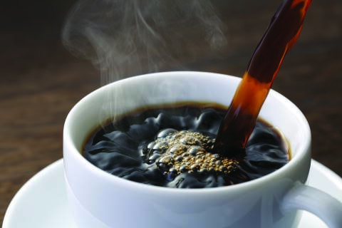 Xícara de café descafeinado ao lado de grãos, representando o processo de extração da cafeína.