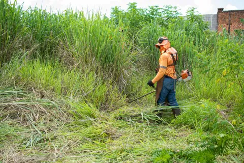 Operador realizando limpeza de terreno com roçadeira e EPIs de segurança.