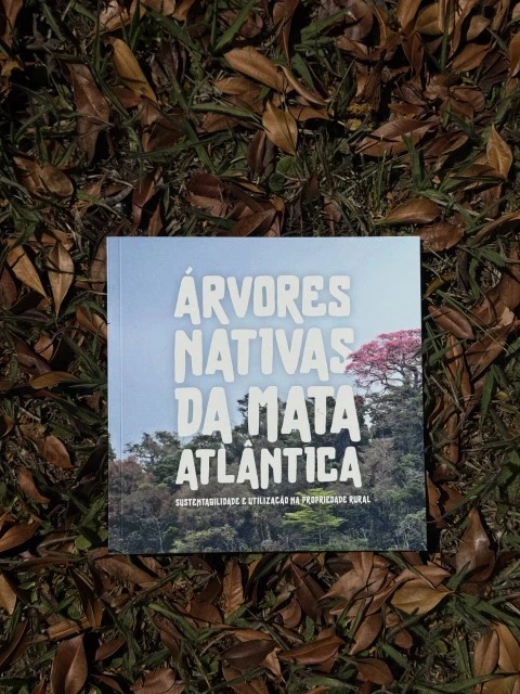 Cartilha da Mata Atlântica com mudas nativas ao fundo.