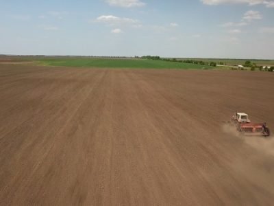 Farmer in tractor preparing land with seedbed cultivator as part of pre seeding activities in early spring season of agricultural works at farmlands. Drone photo