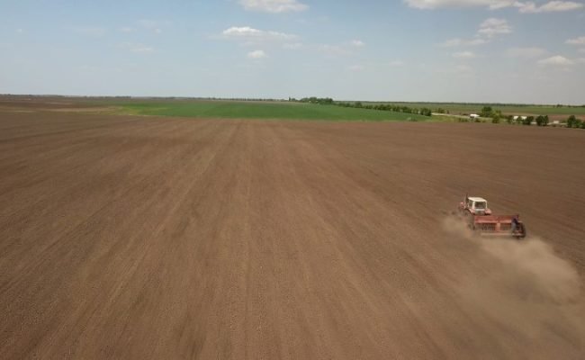 Farmer in tractor preparing land with seedbed cultivator as part of pre seeding activities in early spring season of agricultural works at farmlands. Drone photo