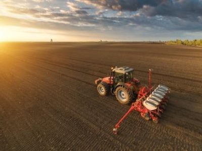 Farmer with tractor seeding - sowing crops at agricultural field in spring