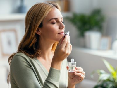 Shot of a beautiful woman holding a bottle of essential oil while testing it sitting on a couch at home.