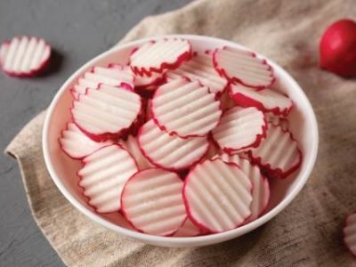 Fresh Radish Chips Slices in a white bowl on a gray background, low angle view. Close-up.