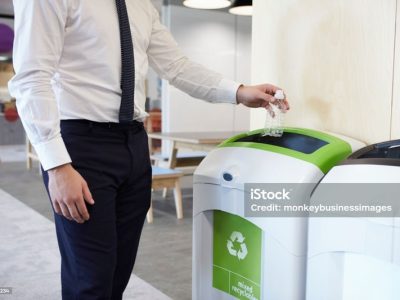 Man in an office throwing plastic bottle into recycling bin