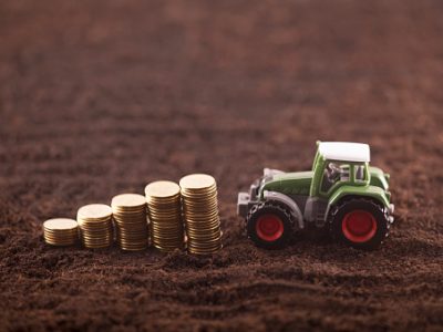 Tractor miniature with coins on fertile soil land