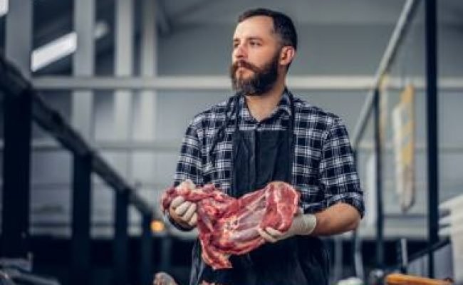Portrait of a bearded meat man holds fresh cut meat.